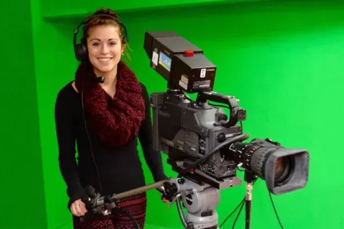 A student controls professional video equipment in front of a green screen