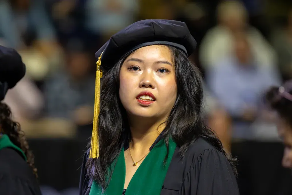 A U N E graduate student in her regalia while looking to the stage