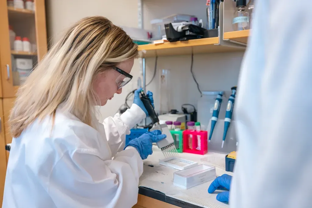 A female U N E student pipetting samples in Sri Mohan's research lab