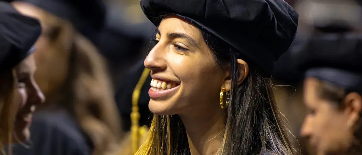 A graduate student in a tam smiles at U N E Commencement